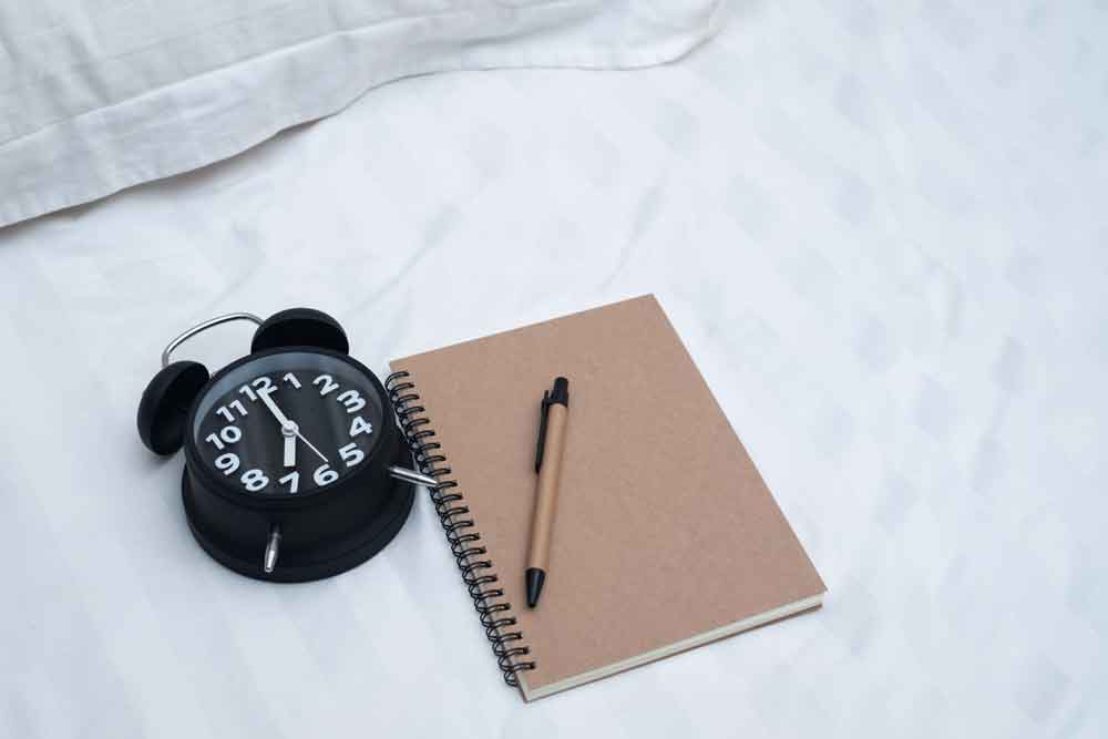 Dream diary or notebook and vintage alarm clock on bed in bedroom.
