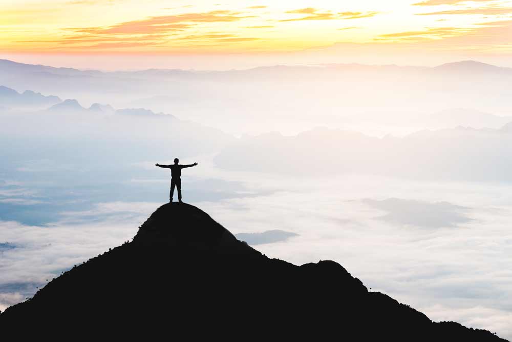 Goals success raising arms stand on top of hill.
