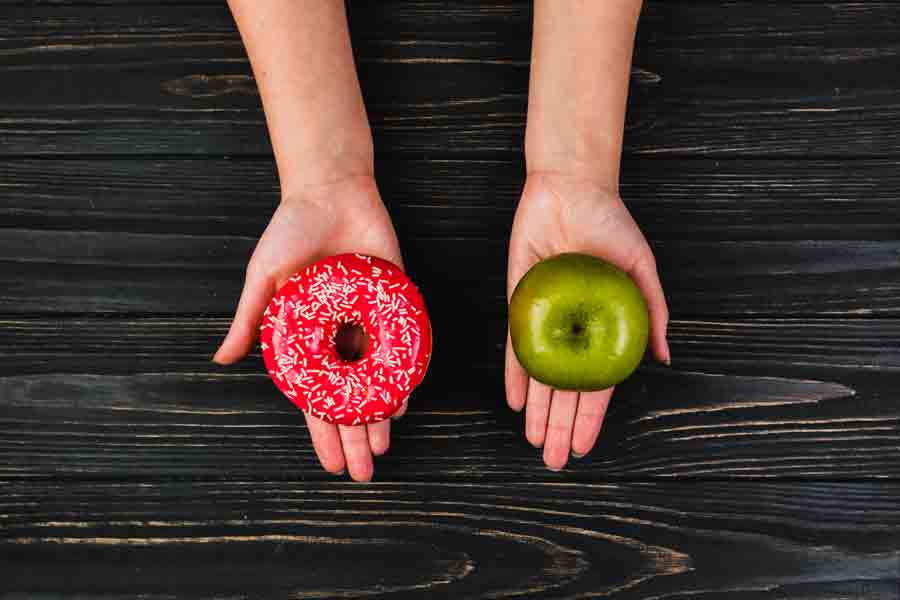 Sebuah potongan tangan memegang donat dan apple.