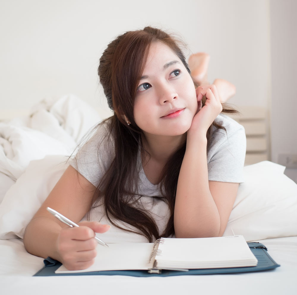 Mujer bonita feliz y relajada escribiendo un diario reflexivo en su cama.