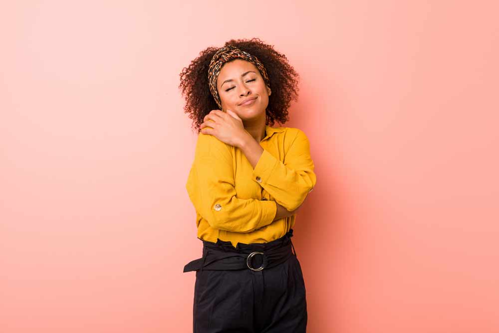 Jovem mulher afro-americana contra um rosa abraços, sorrindo despreocupada e feliz