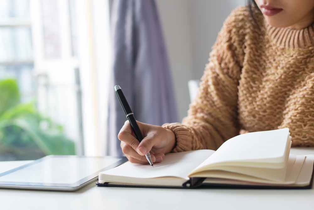 Primer plano de una mujer pensativa escribiendo ideas en un diario.