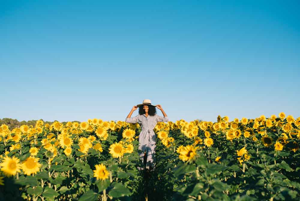 A happy young black woman walking in a sunflower field.