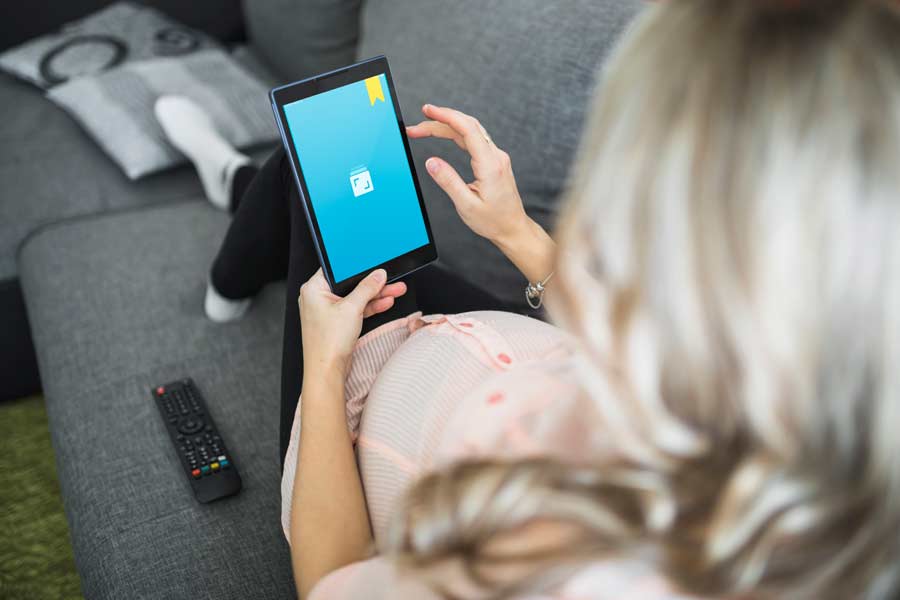 A pregnant woman lying on a couch and using Journey on a tablet.