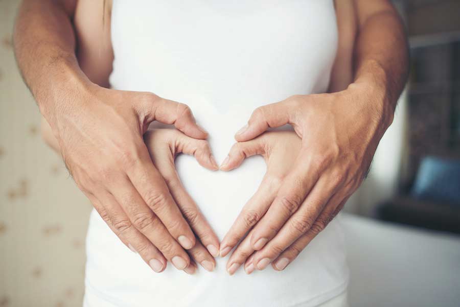 Mujer embarazada y la mano de su esposo mostrando una forma de corazón.