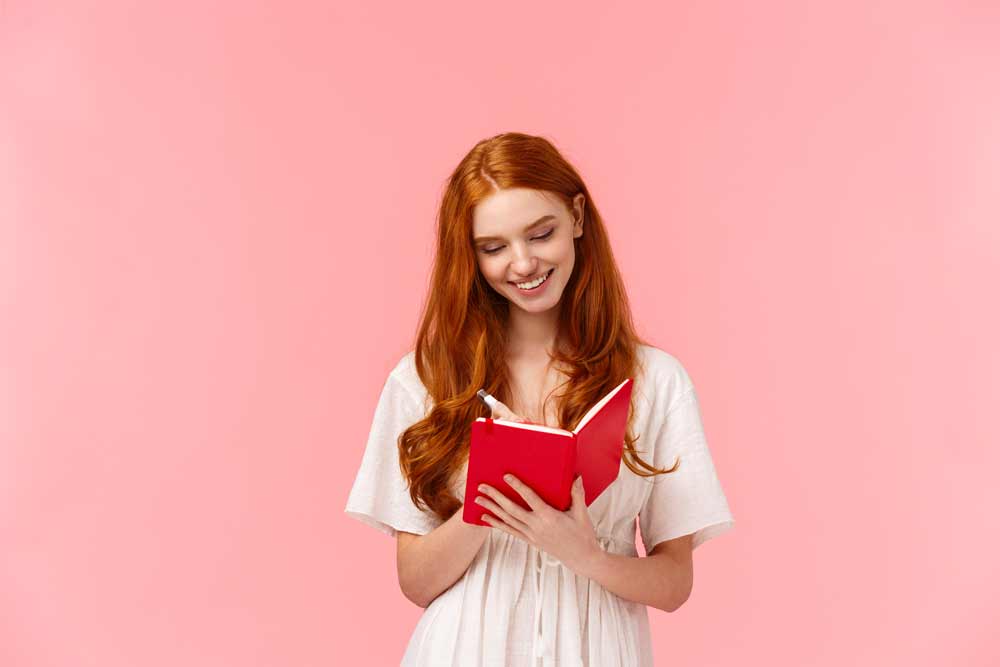 Redhead girl writing on red journal notebook.